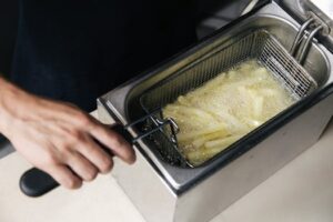 A hand operates a deep fryer cooking fresh french fries in oil.